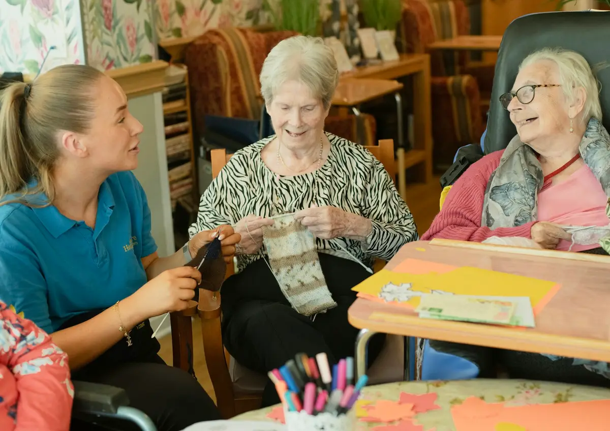 A carer and residents knitting together around a table