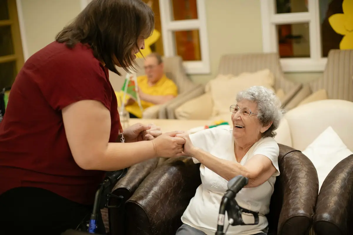 A carer holding the hands of a smiling elderly lady