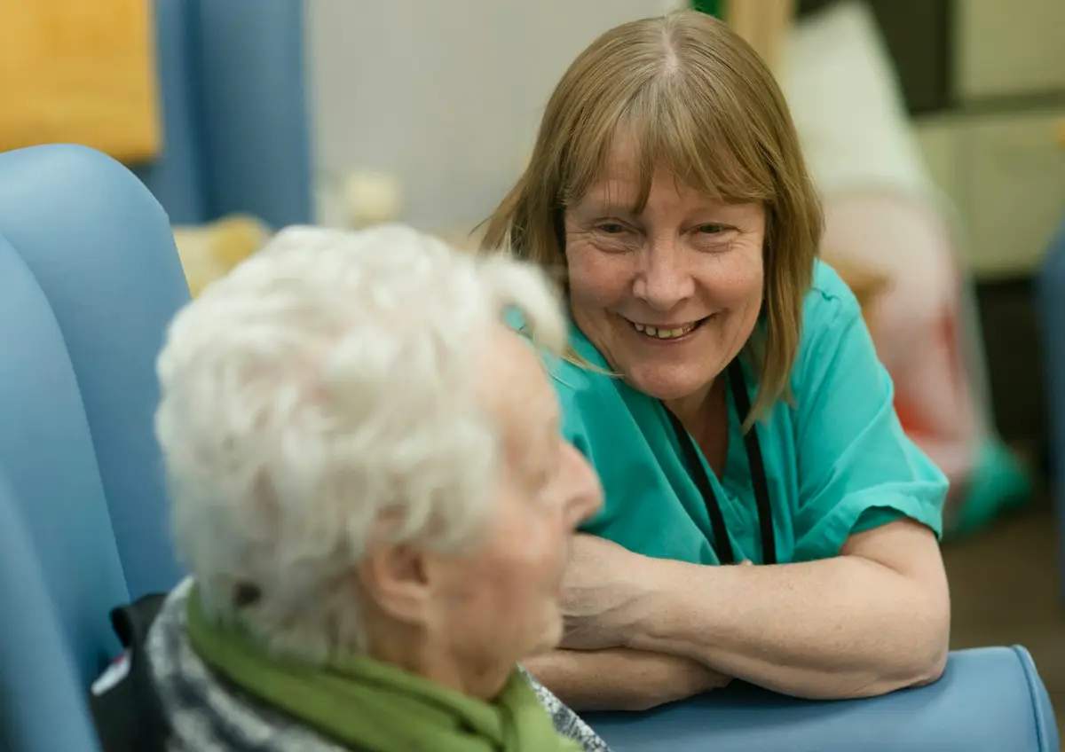 A nurse in green scrubs smiling and talking with an elderly resident
