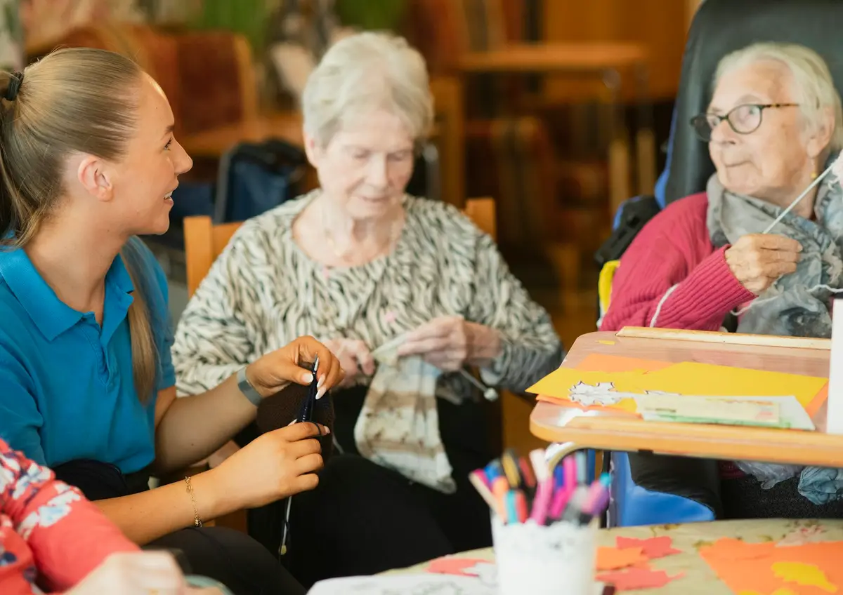 A carer helping residents with a knitting activity