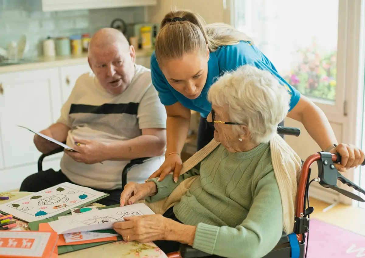 A carer helping two elderly residents with a colouring activity