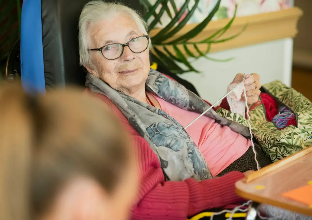 An elderly lady knitting with a soft smile