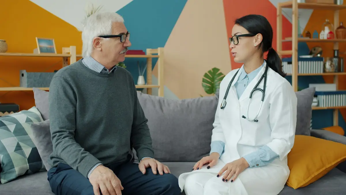 A health professional talking with an older man on a sofa